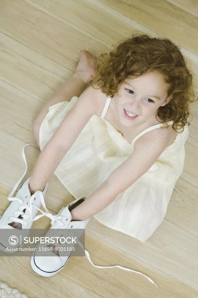 Little girl on floor with hands in shoes, smiling, view from directly above
