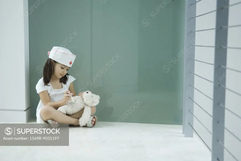 Little girl in nurse hat giving teddy bear shot