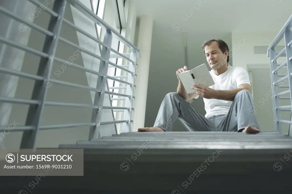 Man sitting on stairs, reading book, low angle view