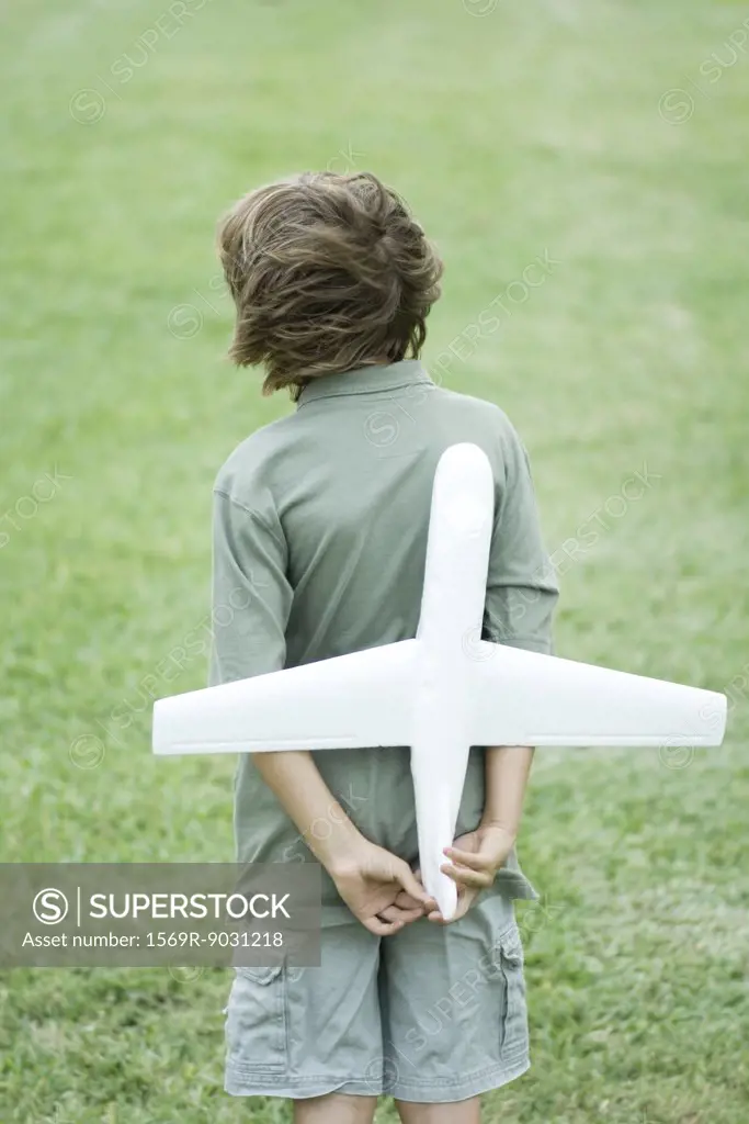 Boy holding toy airplane behind back, rear view
