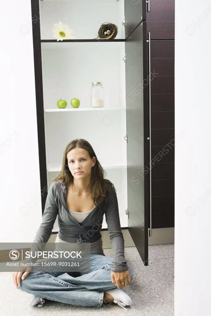 Teenage girl sitting on floor in front of sparse pantry