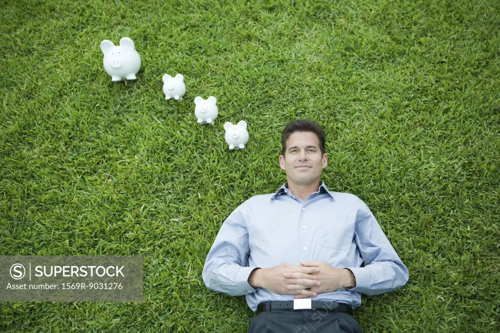 Man lying on grass, smiling, piggy banks by head