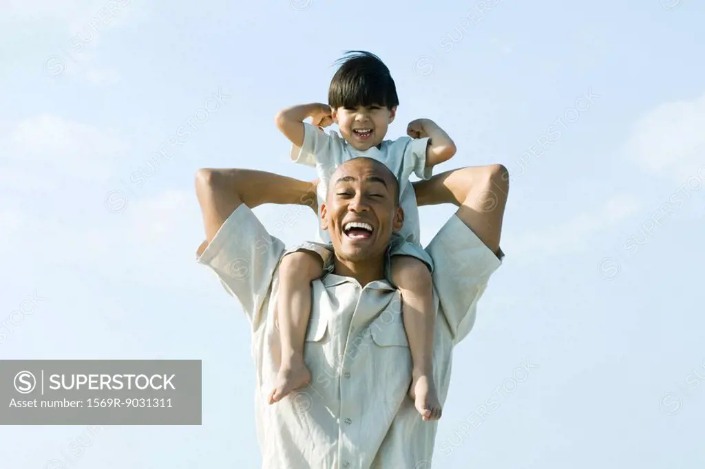 Man carrying son on shoulders, both smiling at camera