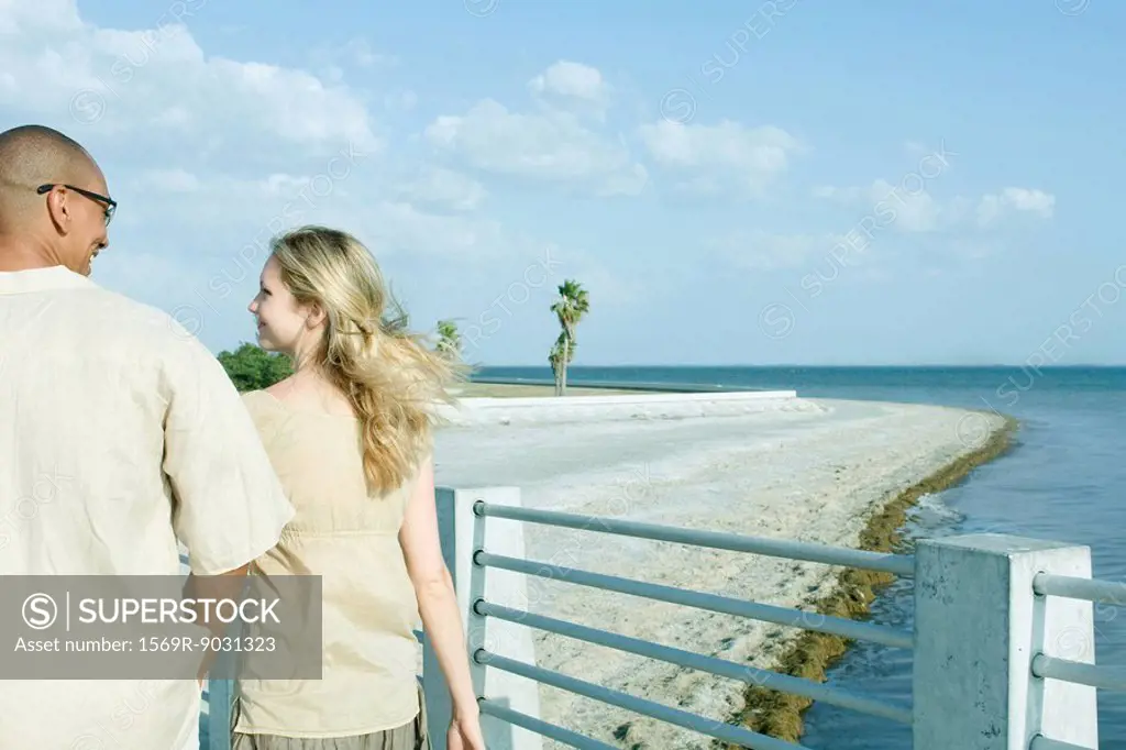 Couple walking together at the beach, looking at each other, rear view