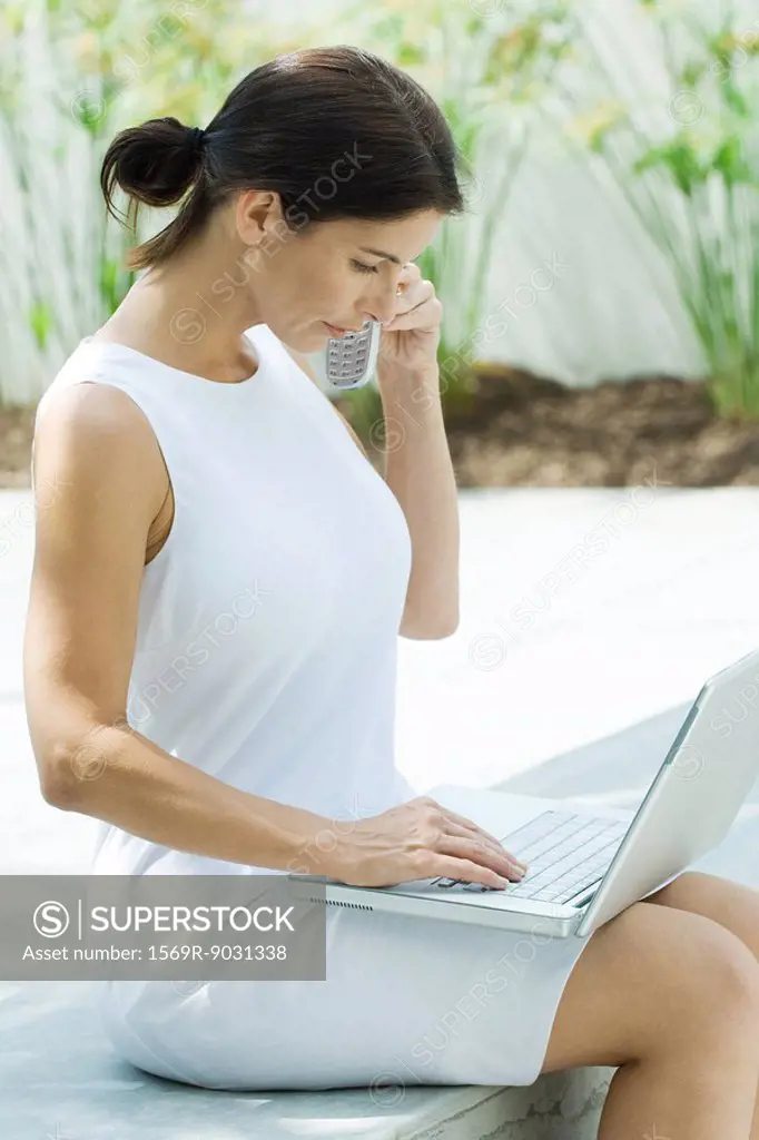 Woman using cell phone outdoors, looking down at laptop computer