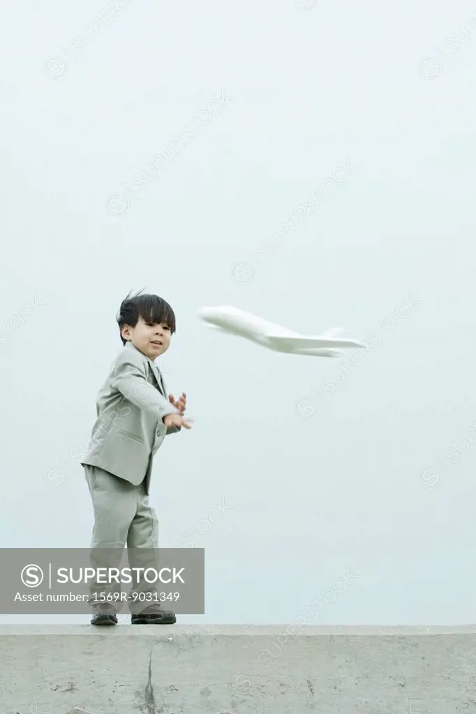 Young boy dressed in suit, throwing toy airplane