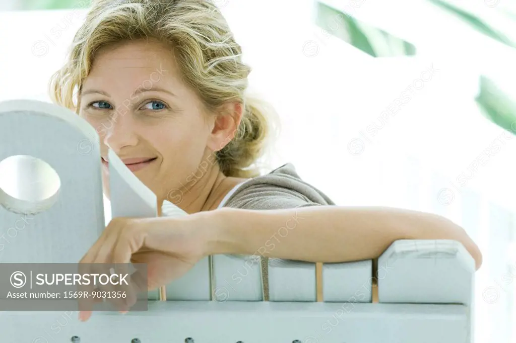 Woman looking over back of bench at camera, smiling