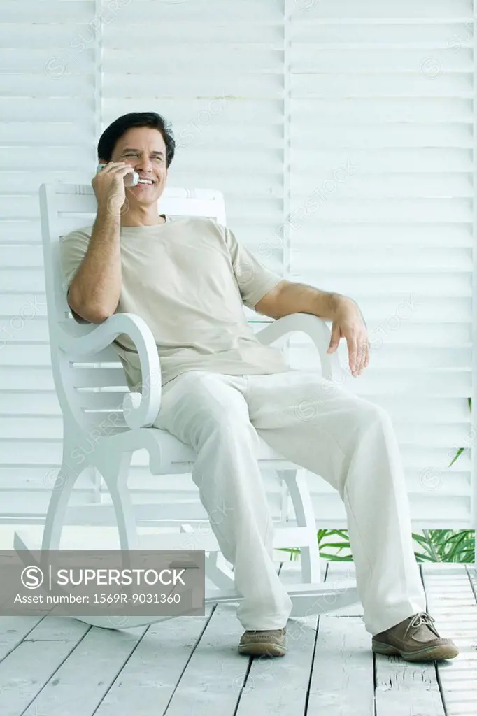 Man sitting in rocking chair, using cell phone, full length