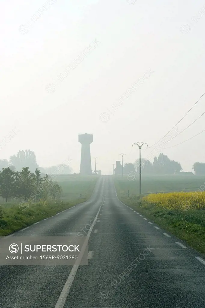 Road and telephone lines in foggy countryside, water tower in the distance