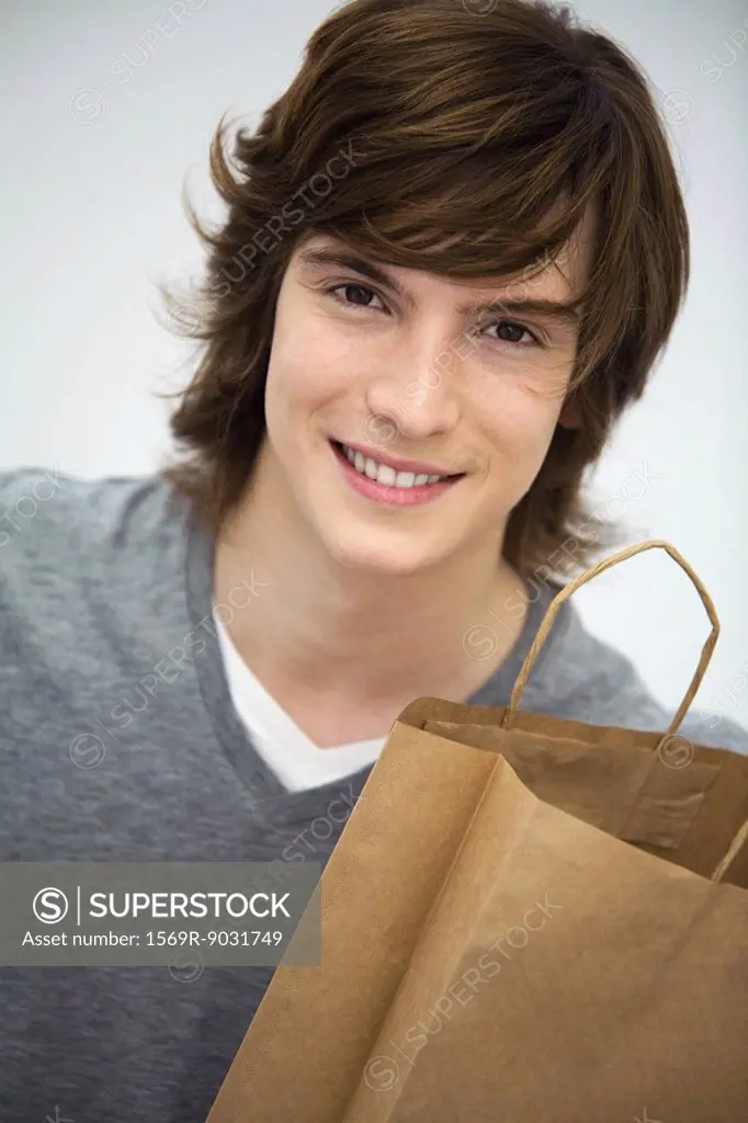 Young man holding shopping bag, smiling at camera, portrait