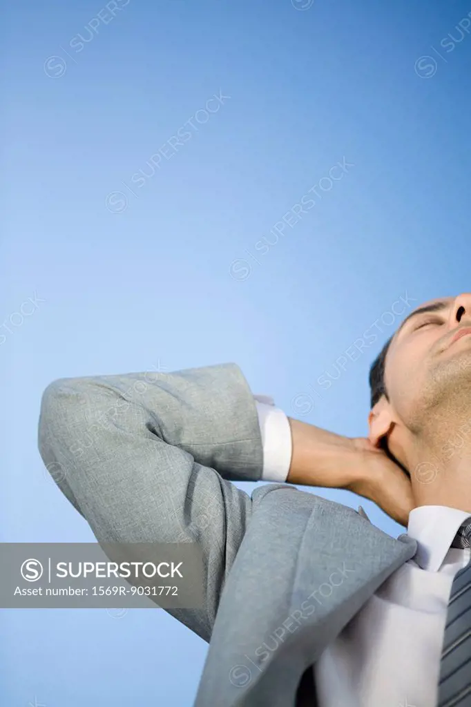 Businessman leaning back, hands behind head, eyes closed, cropped view
