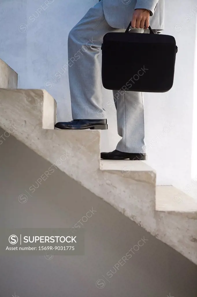 Businessman walking up steps, carrying briefcase, side view, cropped