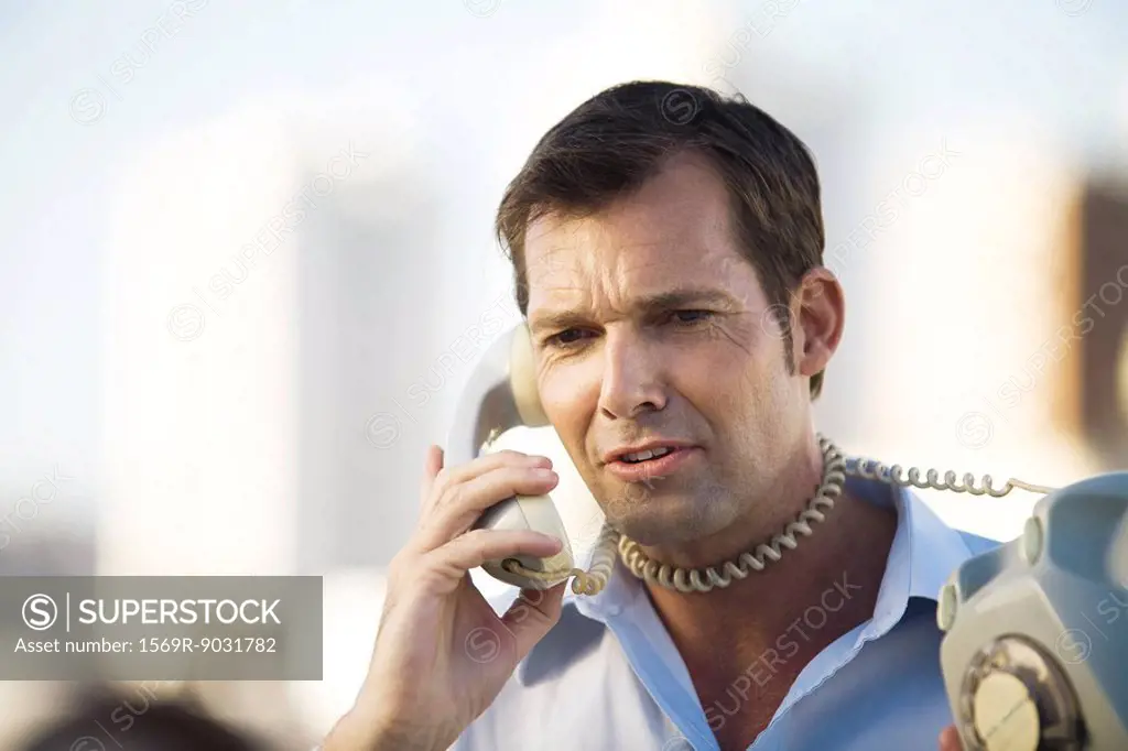 Man talking on landline phone, cord wrapped around his neck, close-up