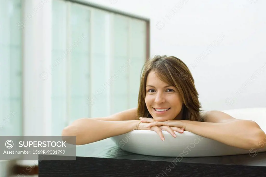 Woman in bathtub, head resting on arms, smiling at camera
