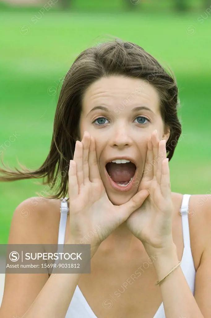Teenage girl shouting, hands raised to mouth, looking at camera