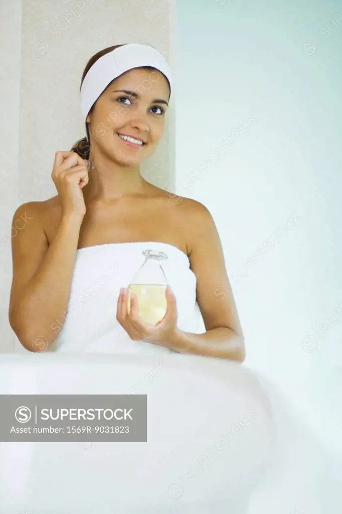 Young woman in towel applying perfume, smiling