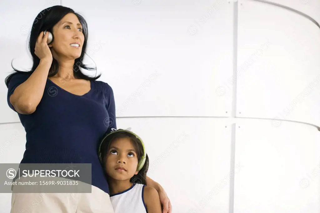 Mother and daughter standing side by side, listening to headphones