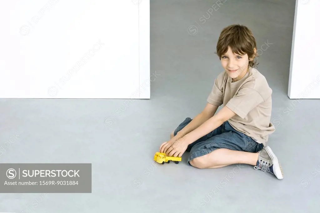 Little boy sitting on the ground, playing with toy truck, smiling at camera