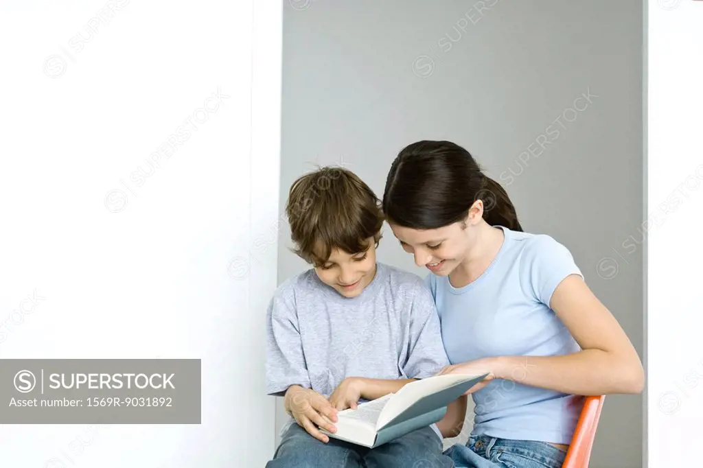 Brother and sister sitting, reading book together, both smiling