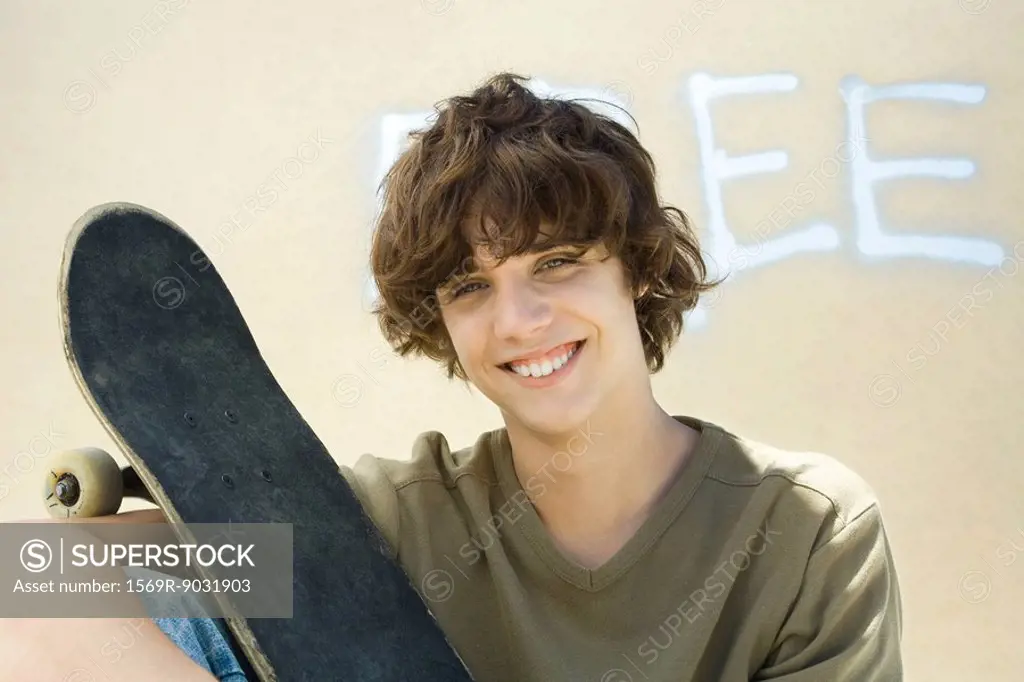 Teenage boy holding skateboard, smiling at camera, portrait