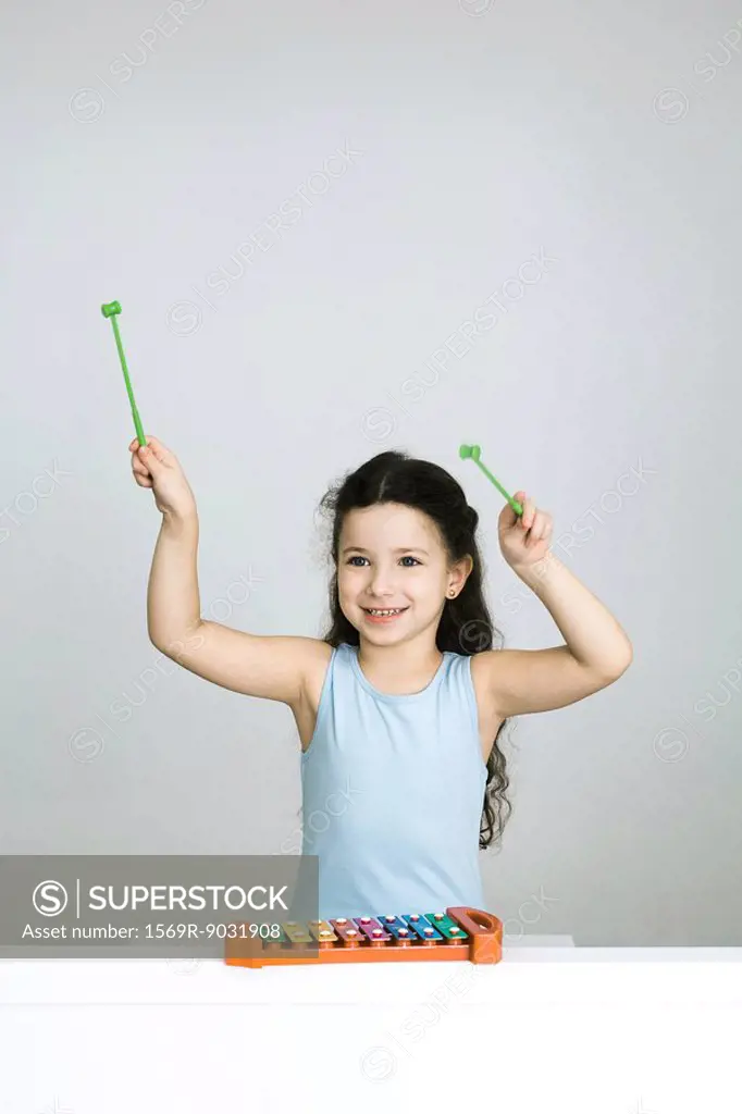Little girl playing xylophone, arms raised, smiling
