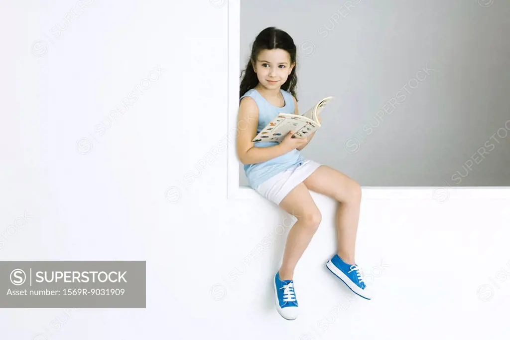 Little girl sitting, holding book, looking away