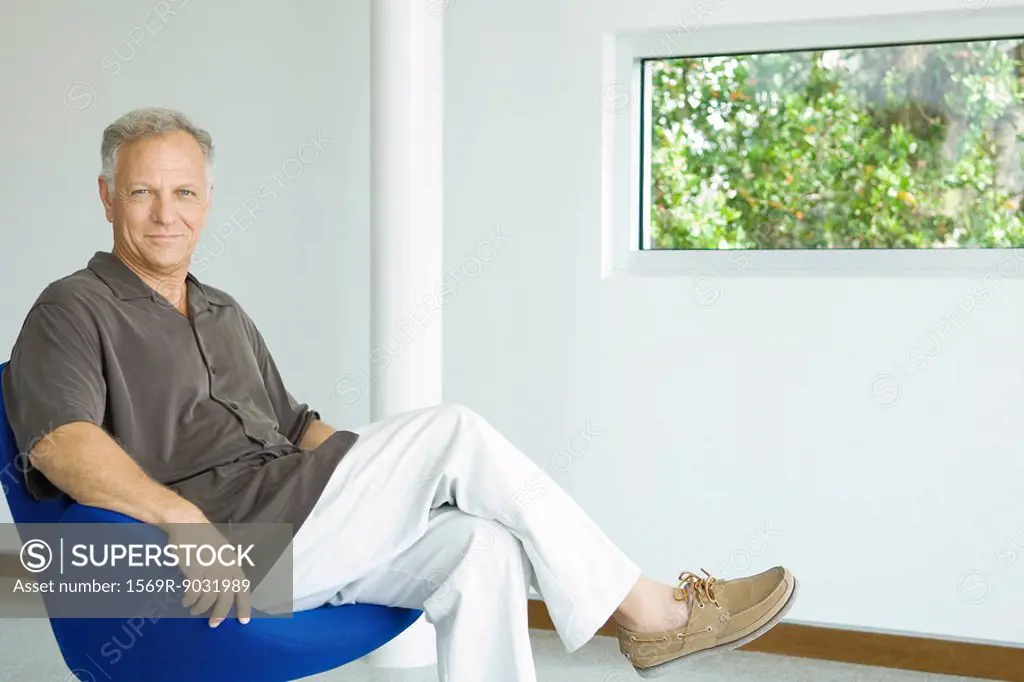Mature man sitting in chair with legs crossed, smiling at camera