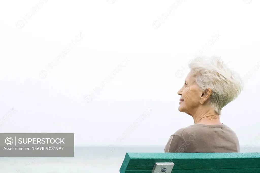 Senior woman sitting on bench, looking up, rear view