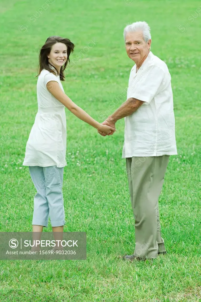 Grandfather and teenage granddaughter holding hands, both smiling over shoulders at camera