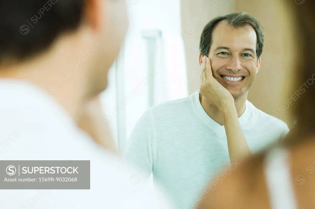 Man with wife´s hand on his cheek, smiling at reflection in mirror, over the shoulder view