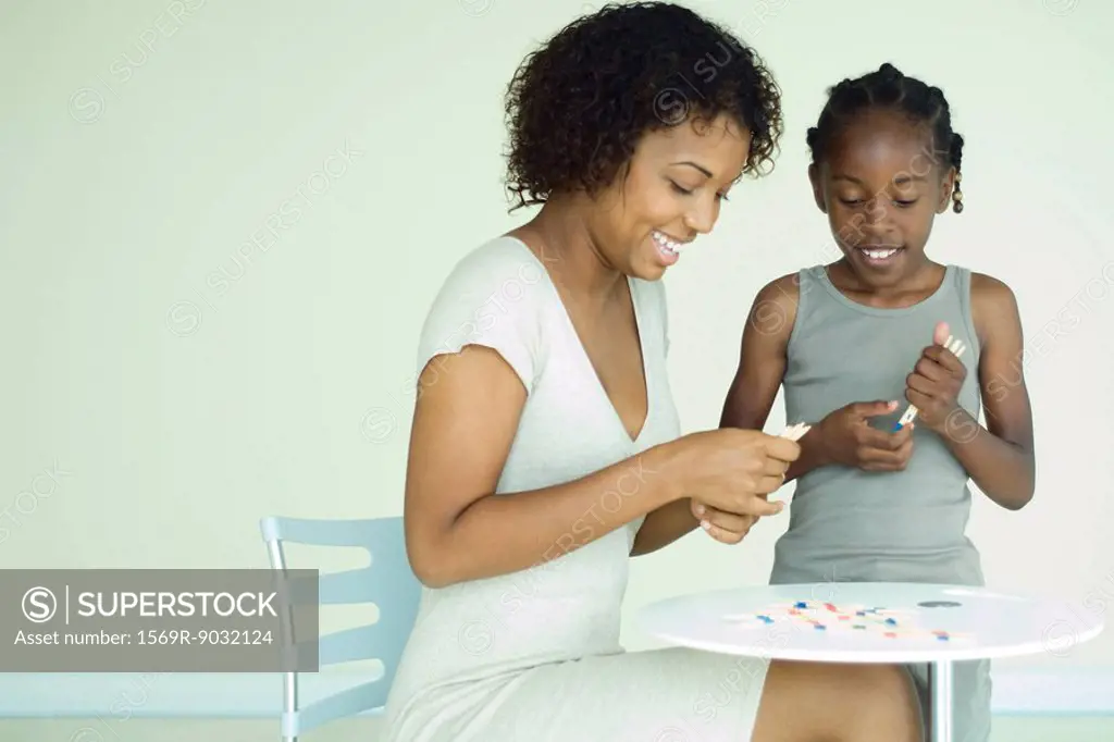 Mother and daughter playing pick up sticks together at table, both smiling