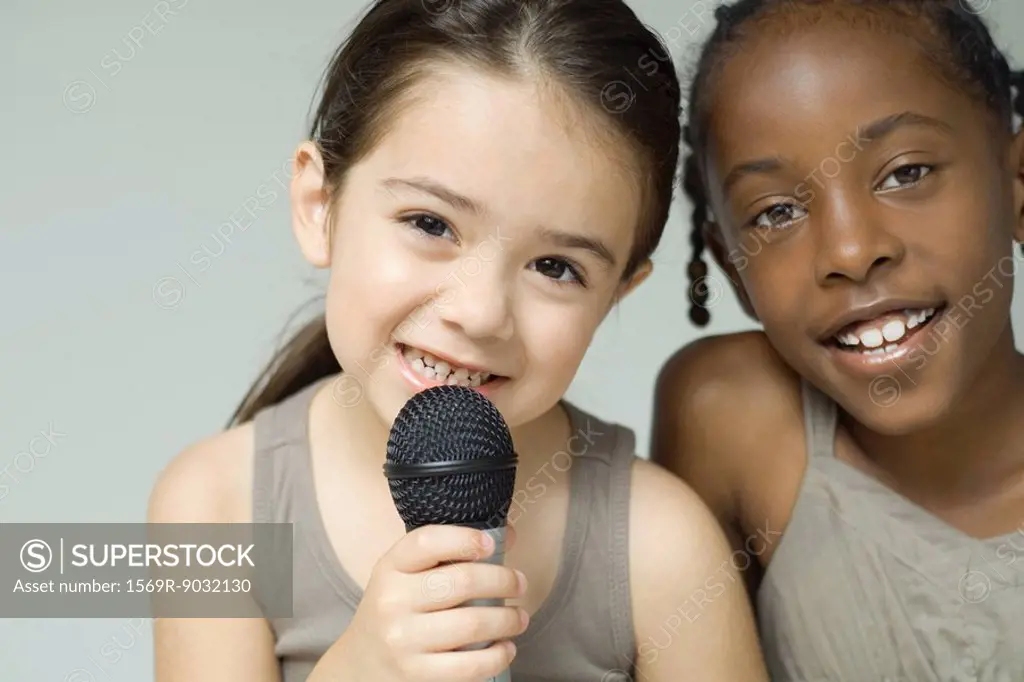 Two little girls smiling at camera together, one holding up microphone