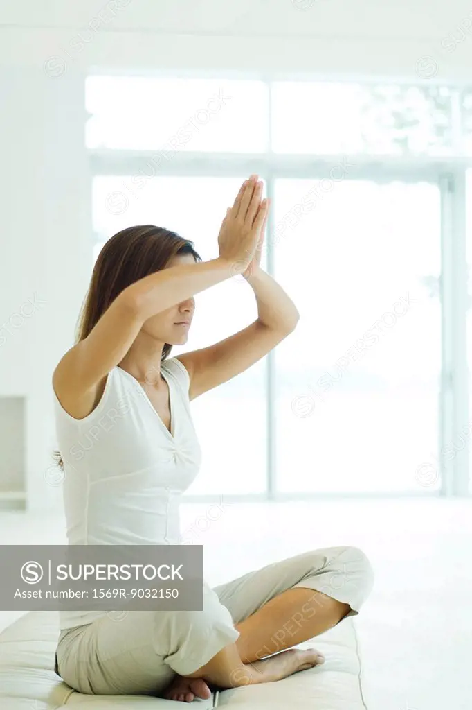 Young woman sitting in lotus position, arms raised, clasped hands