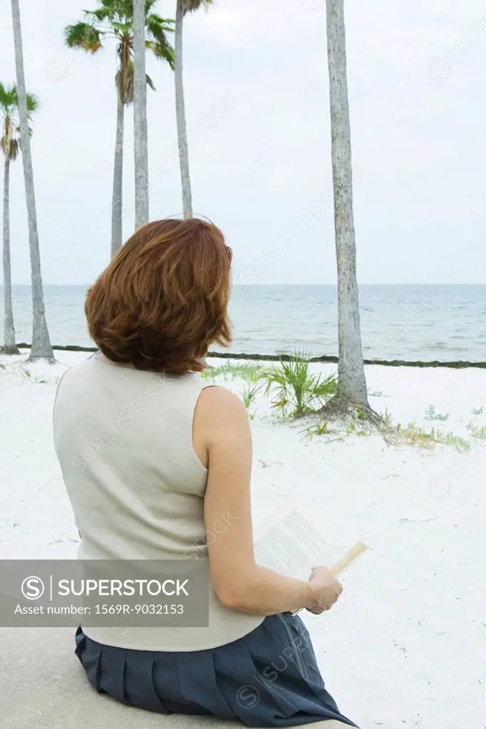 Woman reading book at the beach, rear view