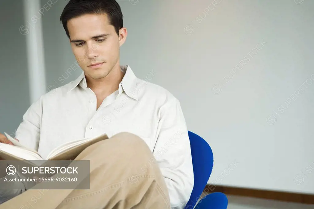 Young man sitting in chair reading book
