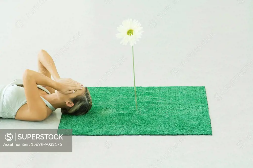 Woman lying with head on square of artificial turf, covering face