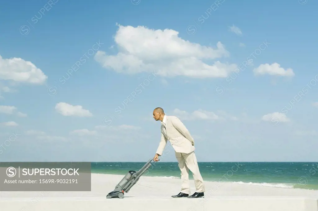 Man in suit using vacuum cleaner on beach, full length
