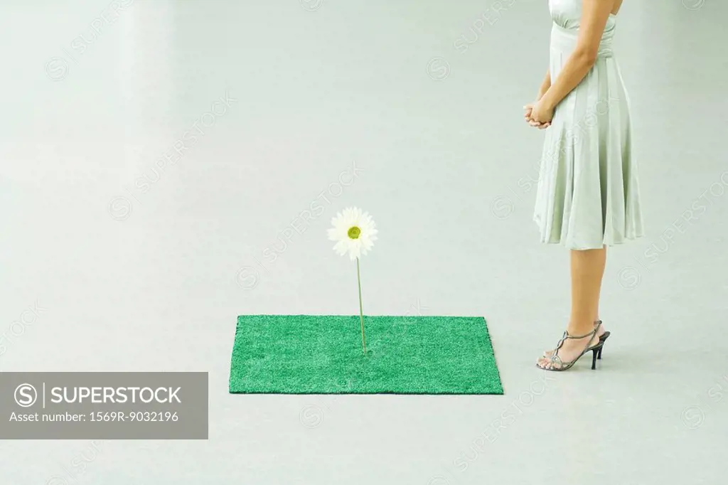 Woman standing by square of artificial turf with fake flower, chest down