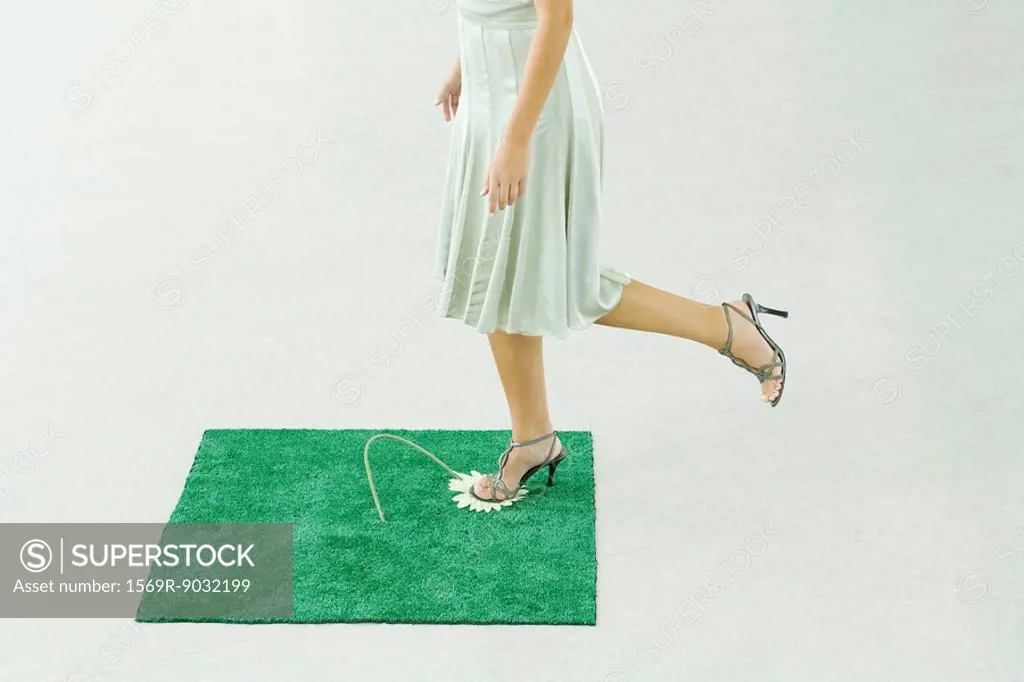 Woman stepping on flower in square of artificial turf, waist down