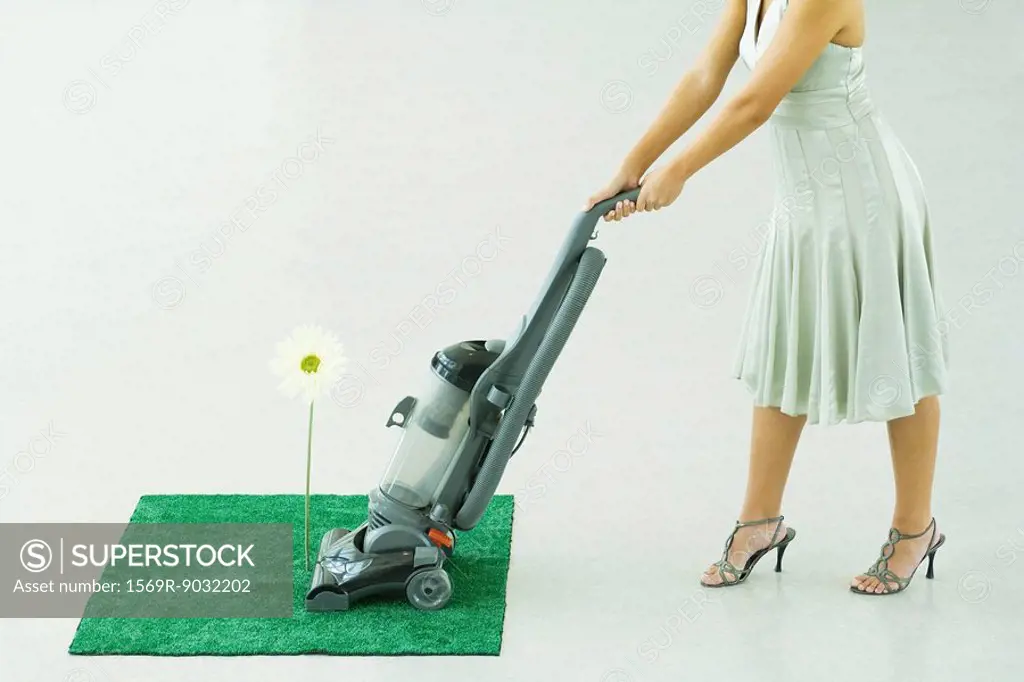 Woman vacuuming square of artificial turf, chest down