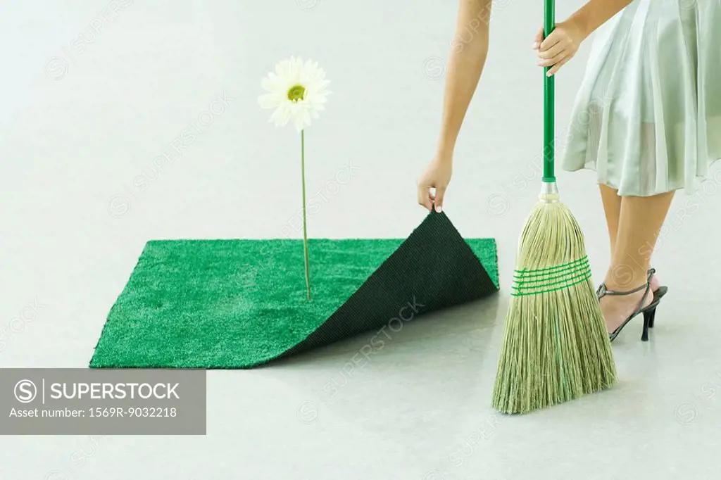 Woman sweeping under artificial turf rug, waist down
