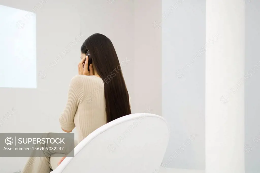 Woman sitting in chair, using cell phone, rear view