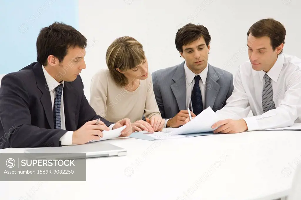 Four business partners sitting together at table, looking at document