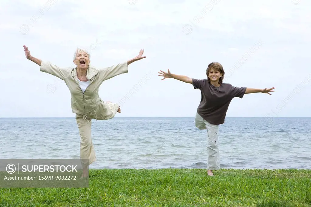 Grandmother and grandson standing on one leg, arms outstretched, both smiling at camera