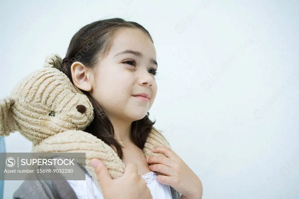 Little girl holding teddy bear on shoulders, smiling, looking away