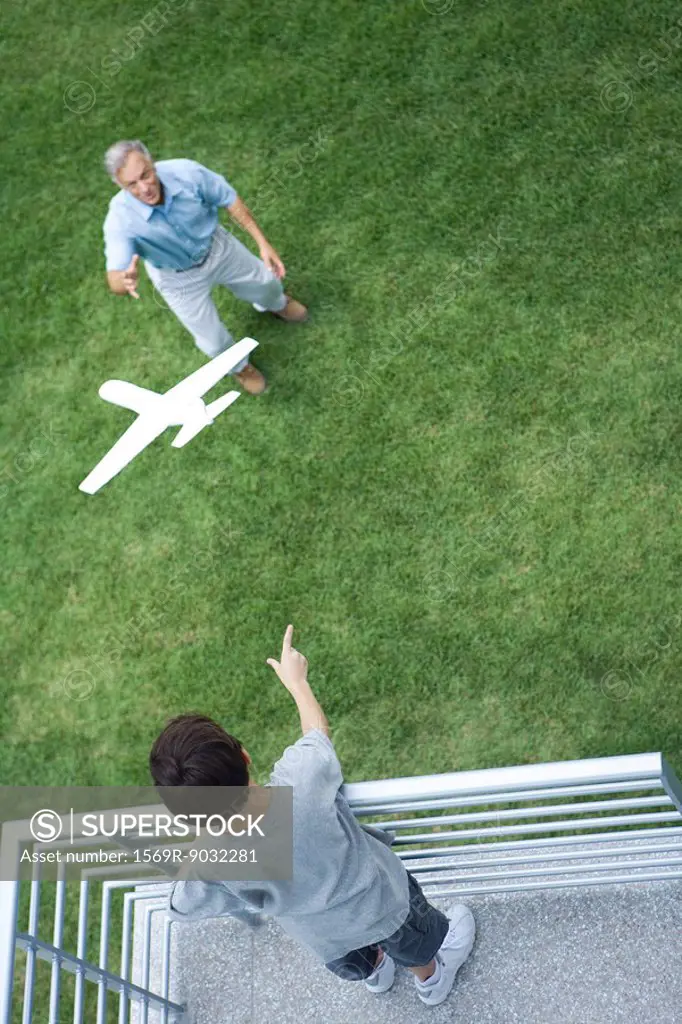 Boy standing on balcony, throwing toy airplane to grandfather standing below, high angle view