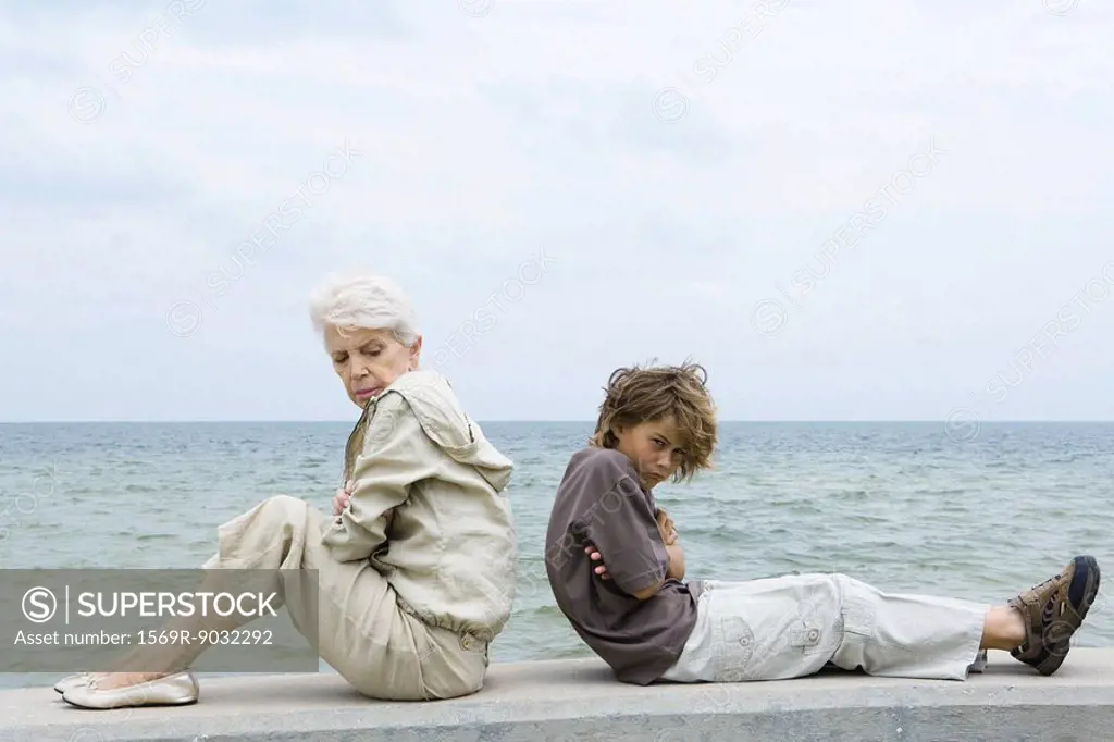 Grandmother and grandson sitting back to back with arms folded, both furrowing brows, side view