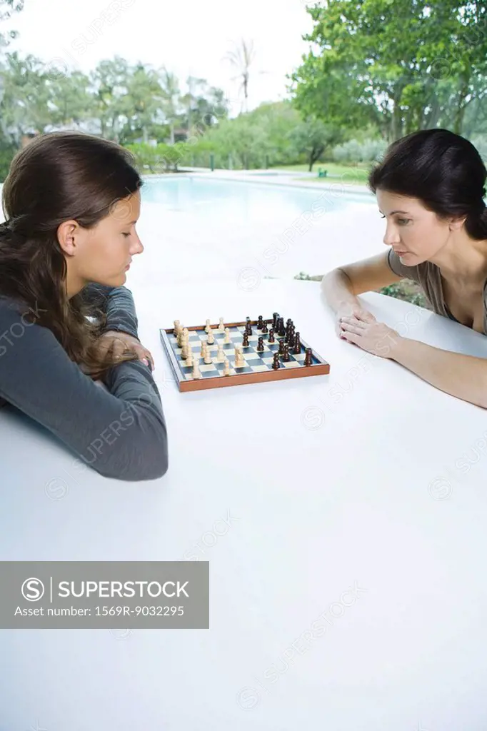 Mother and daughter playing chess together outdoors, side view