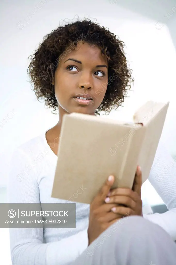 Young woman holding book, looking away, close-up