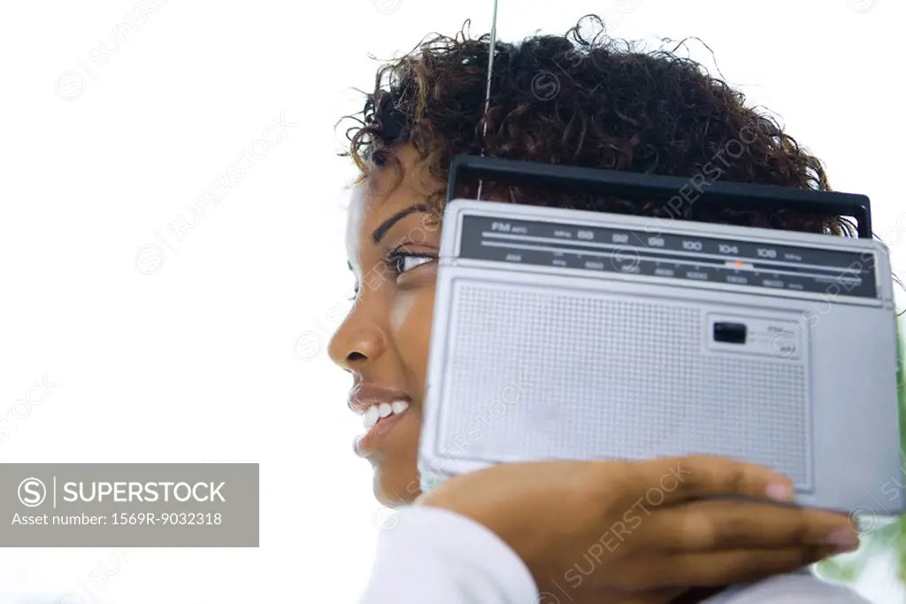 Woman holding radio next to ear, smiling, side view
